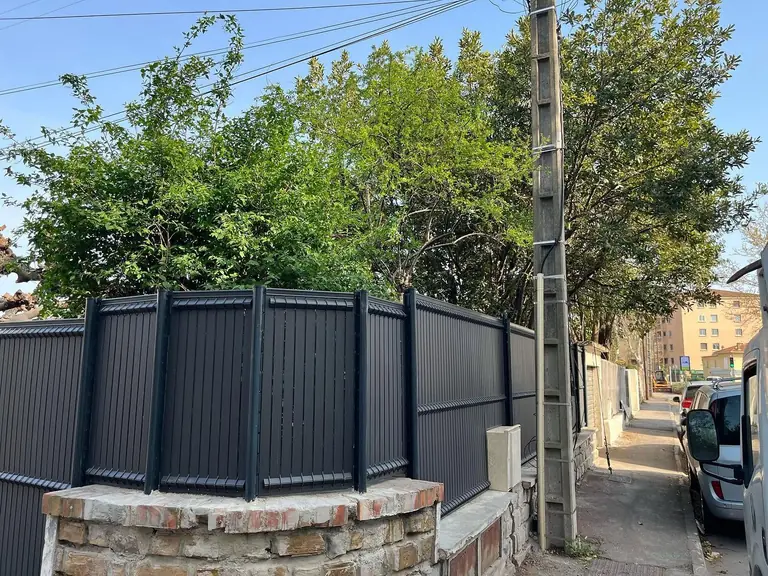 Palissade en lames d’aluminium anthracite posée sur un muret en pierre, à l’angle d’une rue