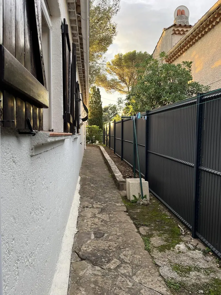Palissade en lames d’aluminium anthracite le long d’une allée dallée, contre une maison
