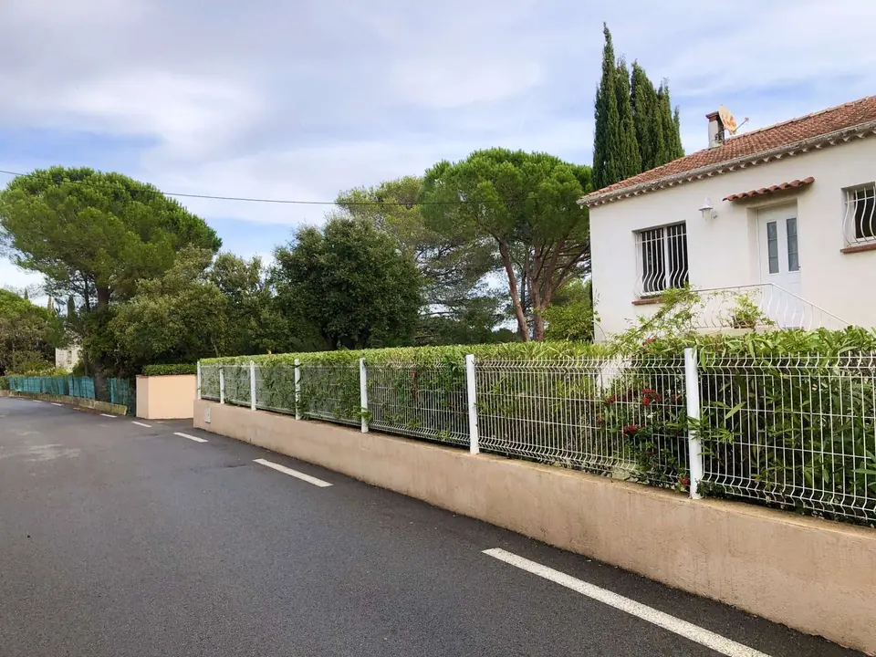 Panneaux rigides blancs sur un muret enduit, haie taillée derrière, devant une villa
